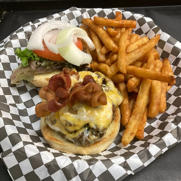 Bacon cheeseburger with lettuce, tomato, onion, and a side of fries in a checkered basket.
