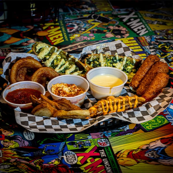 A basket of bar-and-grill appetizers, including fried pickles, onion rings, mozzarella sticks, and dips.