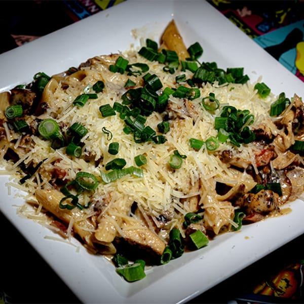 Creamy pasta dish with chicken, mushrooms, shredded cheese, and chopped green onions on a white plate.