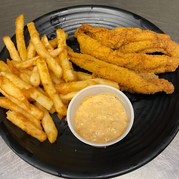 Fried fish fillets, french fries, and a side of dipping sauce on a black plate.