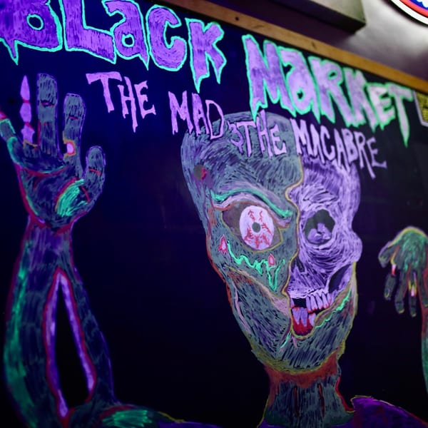 Black Market Bar and Grill sign with a neon zombie drawing and text "The Mad The Macabre".
