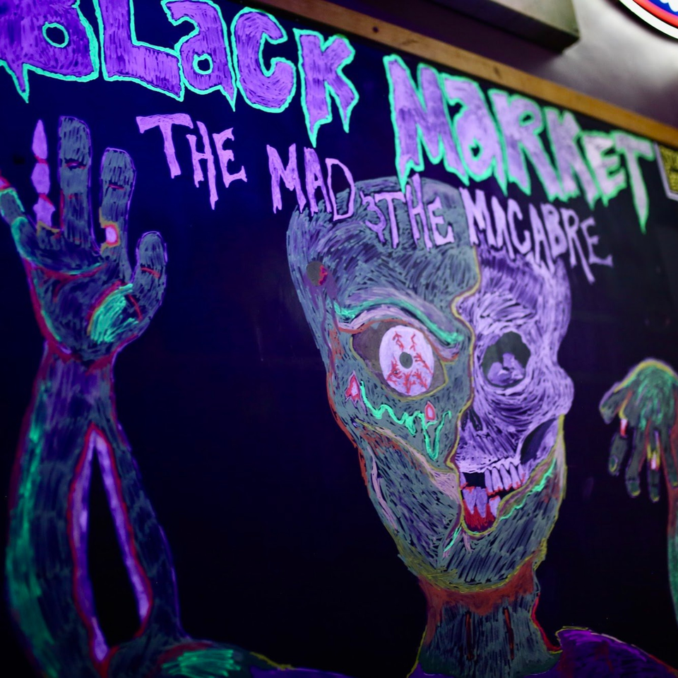 Black Market Bar and Grill sign with a neon zombie drawing and text "The Mad The Macabre".