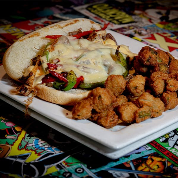 Cheesesteak sandwich with peppers and onions, served with a side of fried okra on a comic book background.