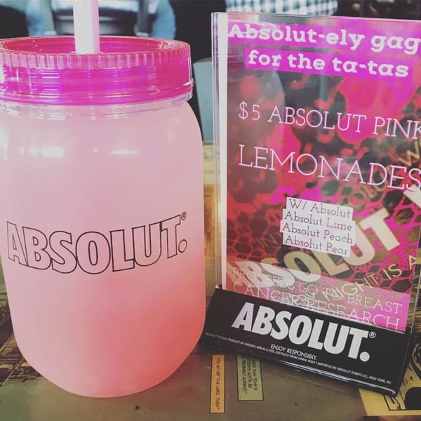 Pink Absolut lemonade in a mason jar with a promotional sign for breast cancer research.