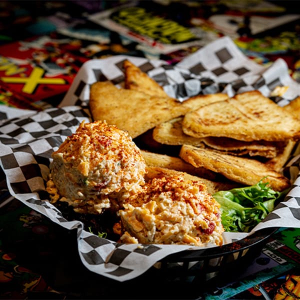 Two scoops of pimento cheese with toasted bread and lettuce in a checkered paper-lined basket.