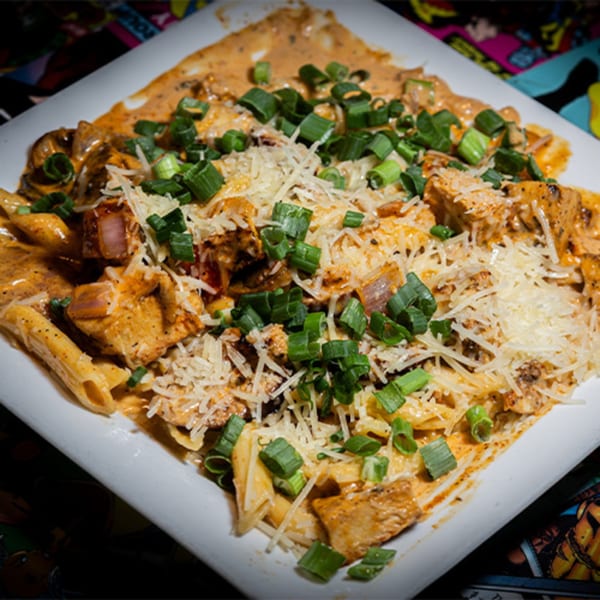 Creamy penne pasta with chicken, mushrooms, parmesan, and green onions on a white plate.