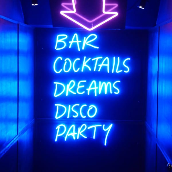 Neon sign with a pink arrow and blue text: BAR, COCKTAILS, DREAMS, DISCO, PARTY.