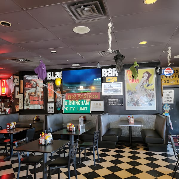 Interior of Black Market Bar and Grill with booths, tables, checkered floor, and eclectic wall decor.