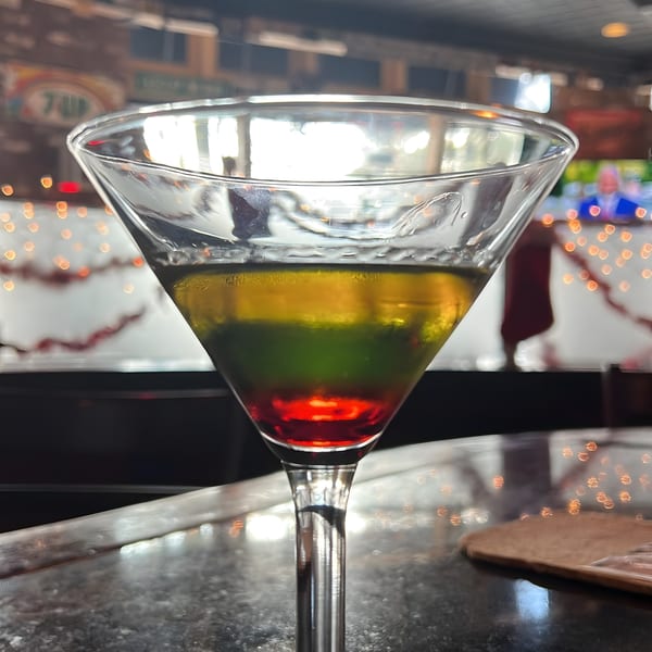 A vibrant, layered cocktail with red, green, and yellow liquids in a martini glass at Black Market Bar and Grill.