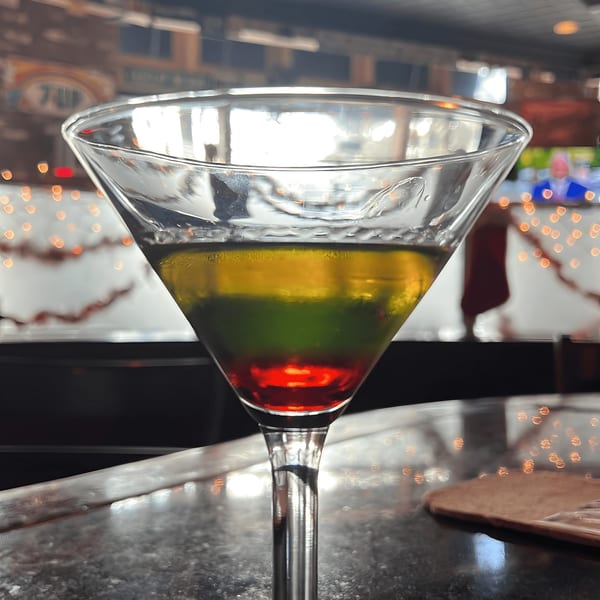 A colorful layered cocktail in a martini glass on a bar at Black Market Bar and Grill.