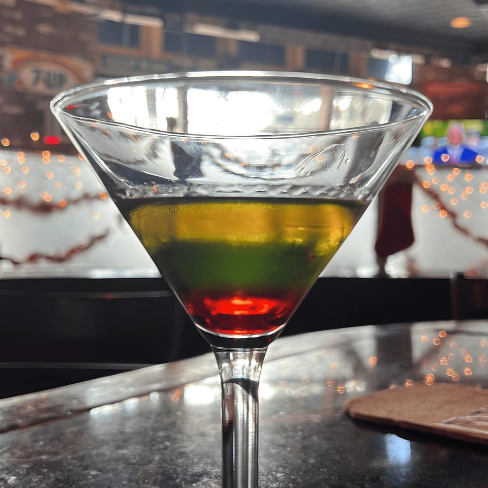 A colorful layered cocktail in a martini glass on a bar at Black Market Bar and Grill.