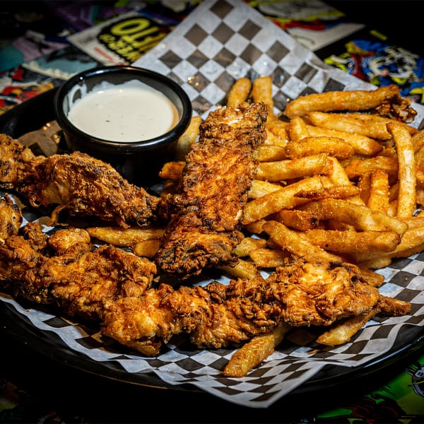 Crispy fried chicken tenders and golden french fries with a side of ranch dressing on checkered paper.
