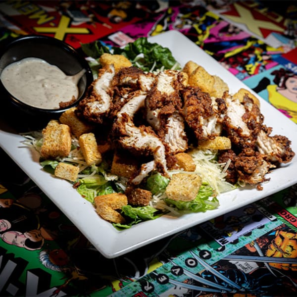 Crispy fried chicken Caesar salad with croutons and a side of dressing on a comic book placemat.