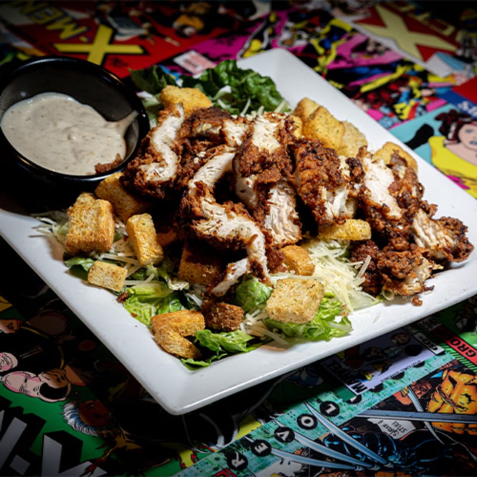 Crispy fried chicken Caesar salad with croutons and a side of dressing on a comic book placemat.