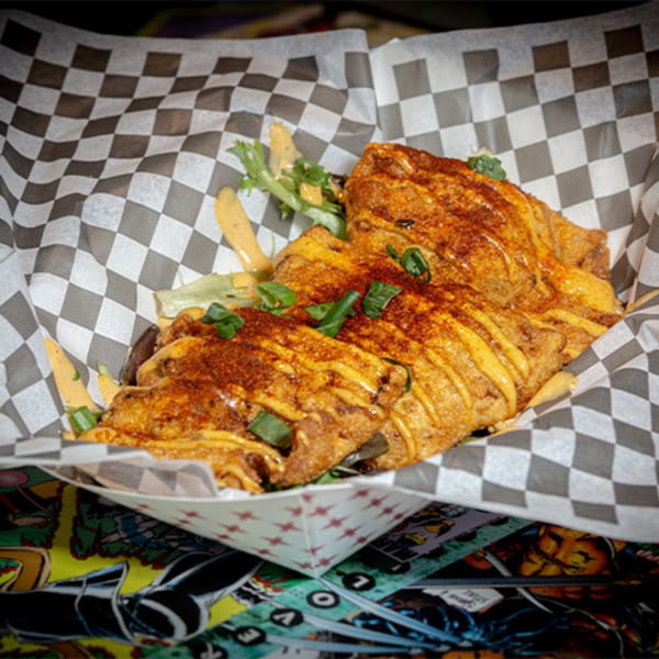 Crispy fried food drizzled with sauce and sprinkled with seasoning and green onions in a checkered paper-lined basket.