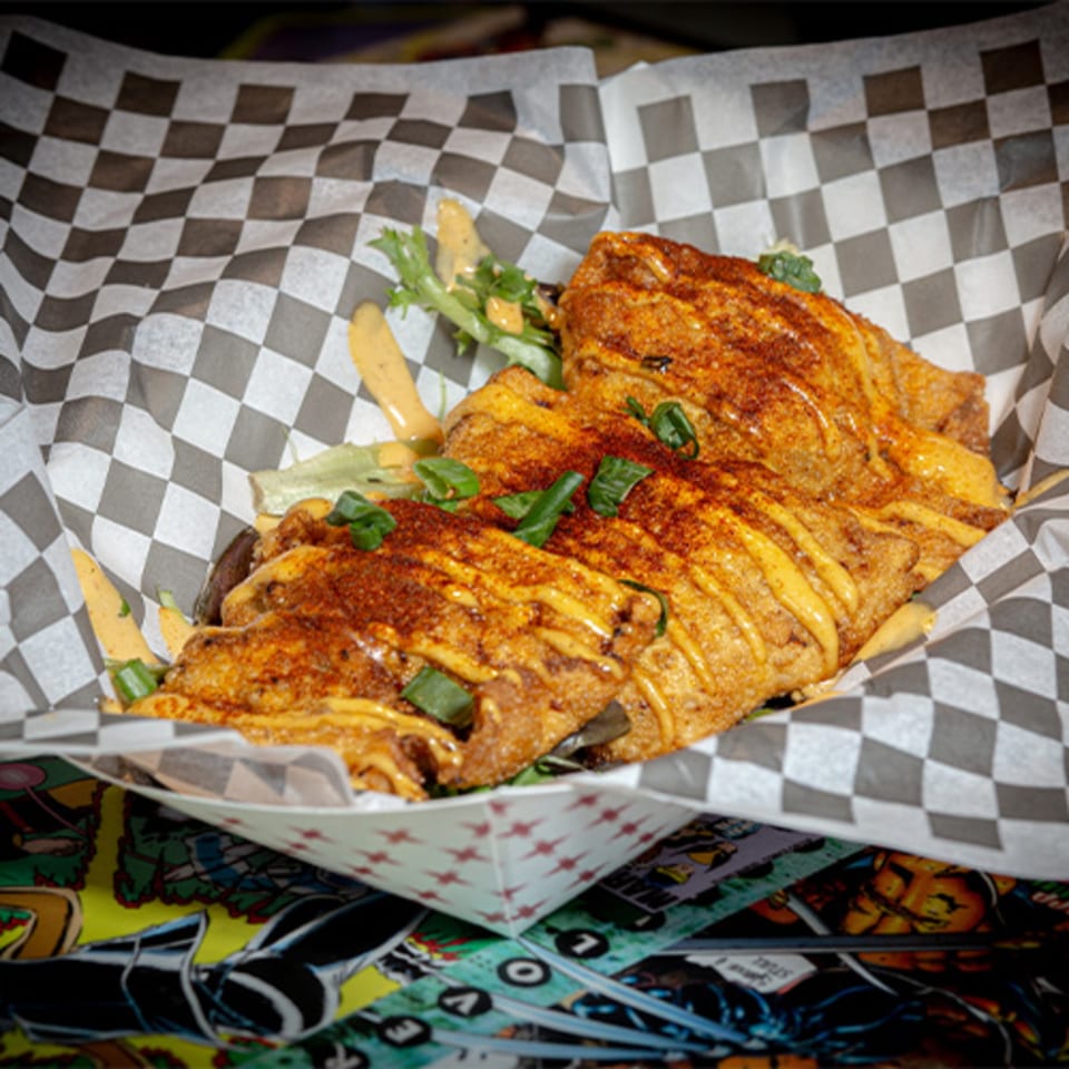 Crispy fried food drizzled with sauce and sprinkled with seasoning and green onions in a checkered paper-lined basket.