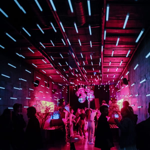 A vibrant, neon-lit bar with blue and red lights illuminating a crowd of people socializing.