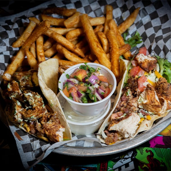 Two chicken tacos with fries and a side of salsa on a metal tray at Black Market Bar and Grill.