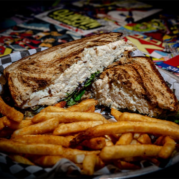 Chicken salad sandwich on toasted bread with fries, served in a basket on a comic book background.